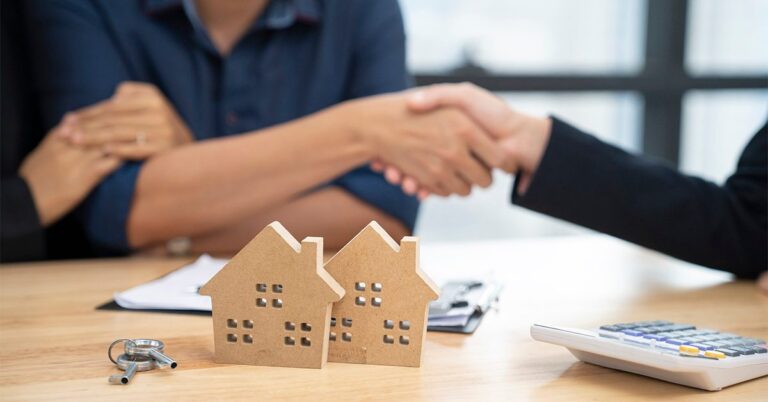 couple shaking hands with business professional wooden houses and calculator on desk gettyimages 1177877358 1200w 628h